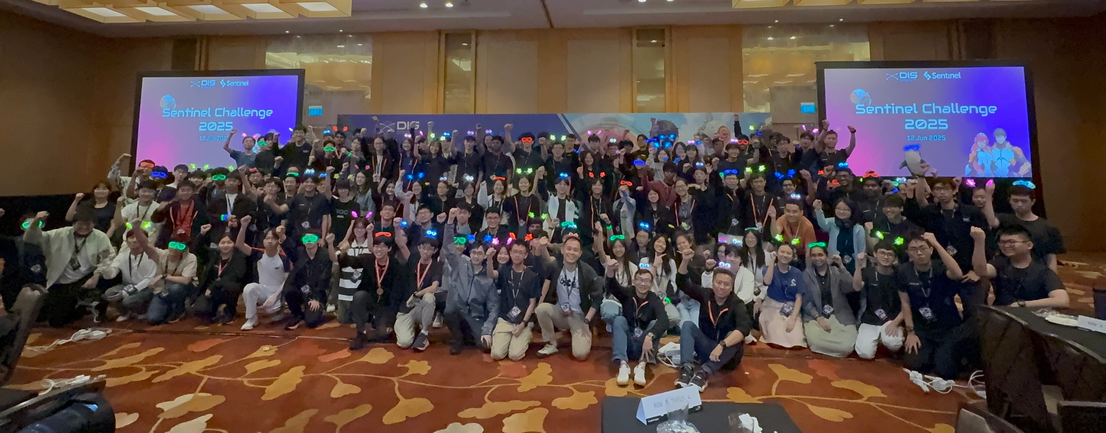 Group photo of participants at the Sentinel Challenge 2025 event with colored headgear and a presentation backdrop.